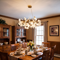 Gold-framed ceramic leaf chandelier above a wooden dining table in a warm, wood-paneled room.