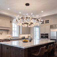 Gold-framed ceramic leaf chandelier above a marble kitchen island with counter stools.